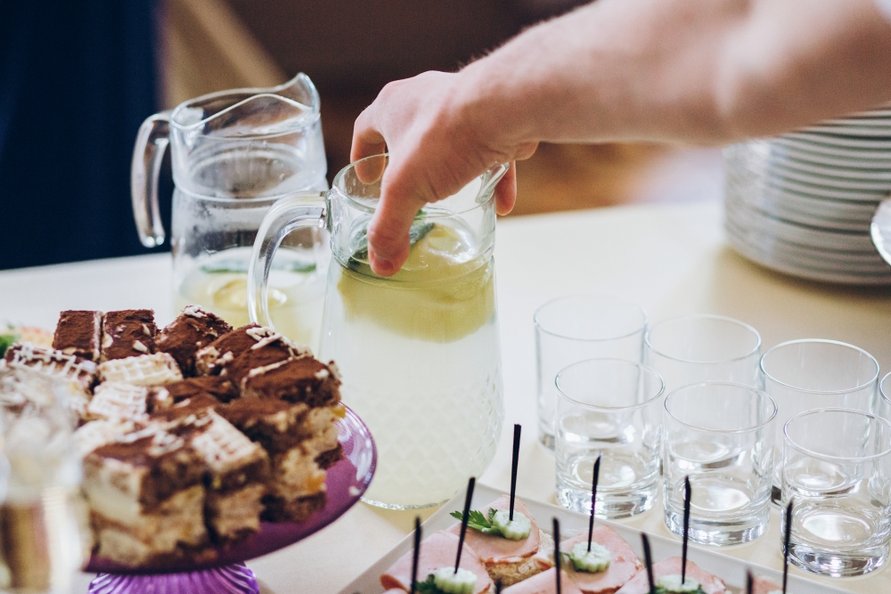 Hände gießen Limonade am Tisch mit Snacks ein.